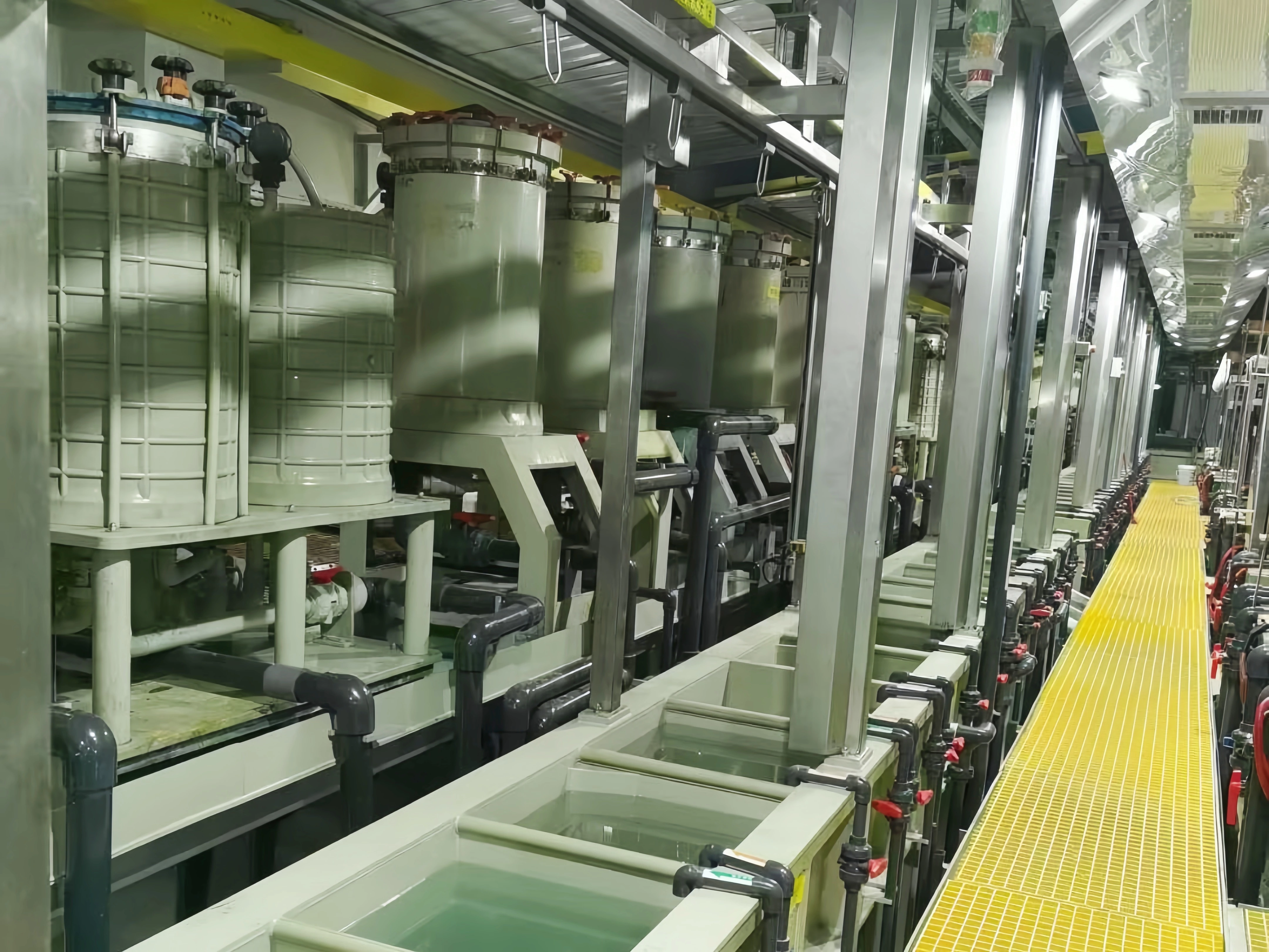 Electroplating tanks and filtration units alongside a yellow service walkway